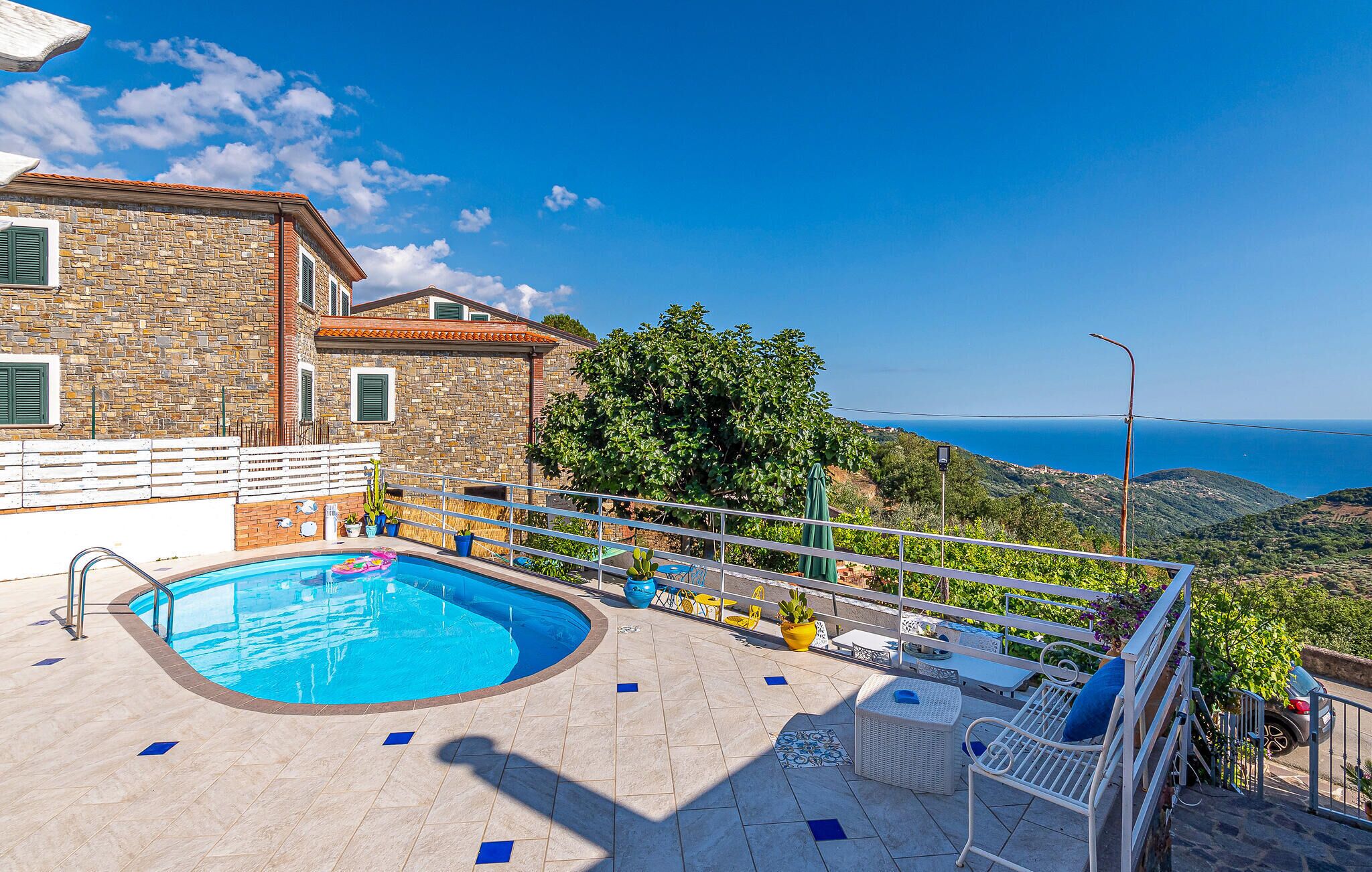 A pool area with a stone building, outdoor furniture, and a view of the sea.