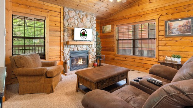 A cozy cabin interior with a stone fireplace, wooden walls, and a comfortable seating area.