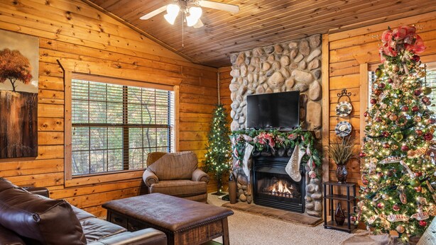 A cozy log cabin interior with a fireplace, a Christmas tree, leather furniture, and a stone wall. - Romantic Studio Cabin Nestled in the Heart of Branson (Branson)