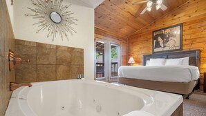 A room with a large bathtub, a bed with white linens, a wooden ceiling, and a wall-mounted artwork. - Romantic Studio Cabin Nestled in the Heart of Branson (Branson)