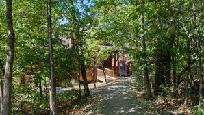 A forested pathway leading to a rustic cabin with a wooden deck and a small porch. - Romantic Studio Cabin Nestled in the Heart of Branson (Branson)