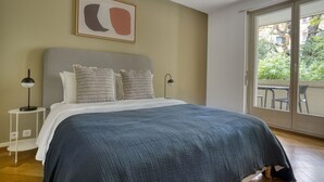 A bedroom with a large bed, two bedside tables, a window with a view of greenery, and a framed abstract painting on the wall. - Sunny St. Alban  3 Room w/ Storage, nr Train Station, by Blueground (Basel)