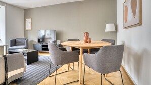 A modern living room with a round wooden table, grey upholstered chairs, a grey sofa, a flat-screen TV, and a lamp. - Sunny St. Alban  3 Room w/ Storage, nr Train Station, by Blueground (Basel)
