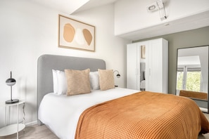 Quarto moderno com uma cama grande, cabeceira cinzenta e guarda-roupa branco.