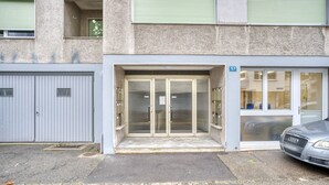 A building entrance with a glass door, a garage door, and a car parked in front.