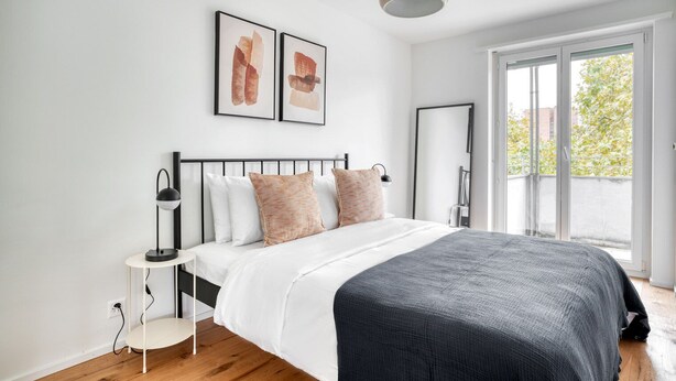 A modern bedroom with a bed, bedside tables, a mirror, and artwork on the wall.