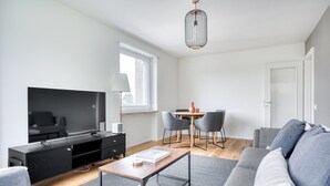 A modern living room with a flat-screen TV, a dining table with chairs, a sofa, and a hanging light fixture.