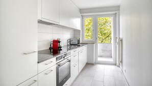 A modern kitchen with white cabinets, a red coffee machine, and a view of trees through a large window.