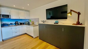 Une cuisine moderne avec des meubles blancs, un four à micro-ondes, un grille-pain et un téléviseur à écran plat fixé au mur.