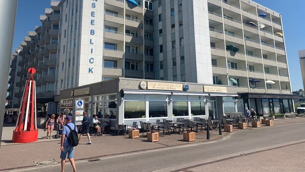 Un hôtel à plusieurs étages, reconnaissable à son enseigne bien visible indiquant « MEERESBLICK », et abritant au rez-de-chaussée un restaurant appelé « DAS MEERESBLICK ».