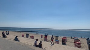 Une plage avec une promenade, des parasols et des gens.