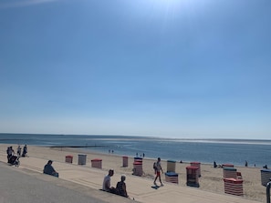 Una playa con un paseo marítimo, sombrillas y gente.