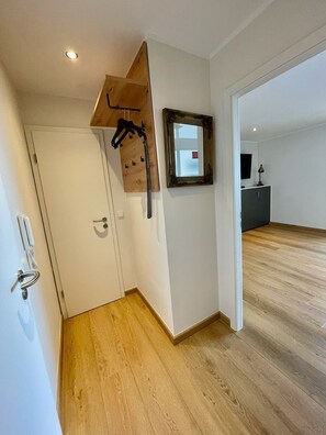 Un pasillo con piso de madera, una puerta blanca y un espejo en la pared.