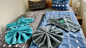 Un lit recouvert d’une couvre-lit à motifs bleus et blancs, deux oreillers à motifs noirs et blancs, et deux serviettes pliées, de couleur turquoise et grise.