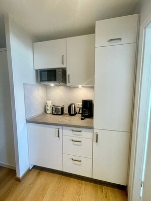 A compact kitchen with white cabinets, a microwave, a kettle, a coffee maker, and a toaster on the countertop. - Strandblick im Haus Seeblick Bismarckstraße 6. Etage - Seeblick (Borkum)