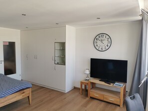 Un dormitorio con cama, armario, mueble para la televisión y un reloj en la pared.