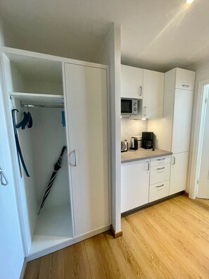 A compact kitchen with white cabinets, a microwave, a coffee maker, and a wooden floor.