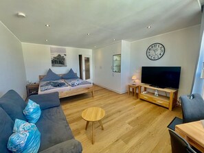 Una sala de estar moderna con un sofá, una mesita redonda, un televisor y un reloj en la pared.