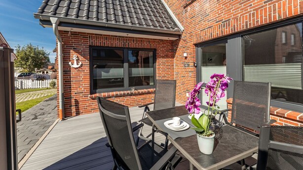 A patio with a table and chairs, a potted orchid, and a brick building with large windows. - Sommerwind Alfonso Borkum Apartment 1 - Vacation with dog - Sommerwind Alfonso (Borkum)