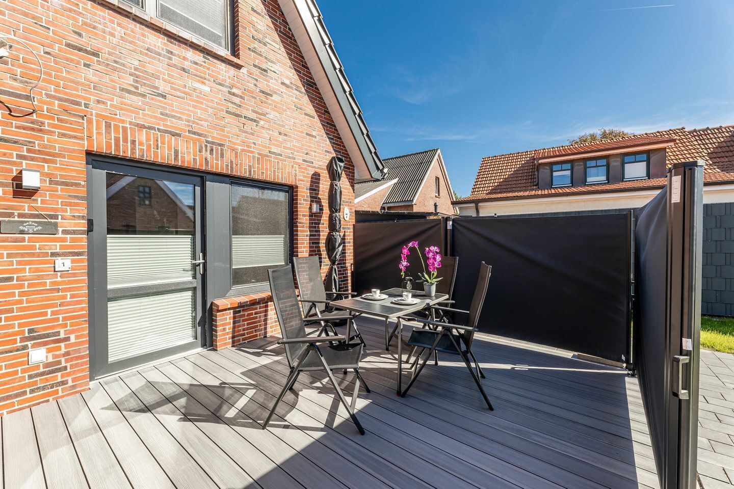 A patio with a table and chairs, a brick wall, and a sliding door.