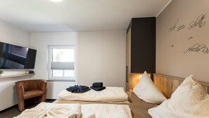 A room with a TV, a chair, two beds with towels, a window, and a wall with text. - Sommerwind Alfonso Borkum Apartment 1 - Vacation with dog - Sommerwind Alfonso (Borkum)