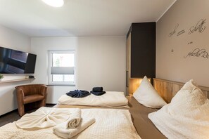 A room with a TV, a chair, two beds with towels, a window, and a wall with text.
