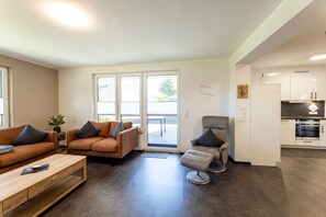 A modern living room with a sofa, armchair, and coffee table. There is a sliding glass door leading to a balcony.