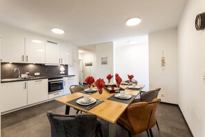 Cozinha moderna com armários brancos e uma mesa de jantar de madeira para quatro pessoas.