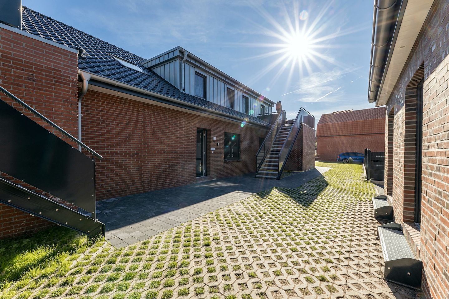 Une cour avec un bâtiment en briques, un escalier et un chemin pavé.