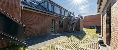 Une cour avec un bâtiment en briques, un escalier et un chemin pavé.