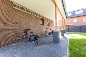 A covered outdoor area with a brick wall, two bicycles, and a trash bin.