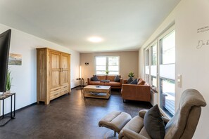 A spacious living room with a large wooden cabinet, a leather sofa, a coffee table, and a television.