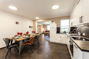 A modern kitchen with white cabinets, a stainless steel countertop, and a dining area with a wooden table and chairs.