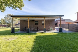 A covered outdoor area with a brick building, a bike rack, and a grassy lawn.