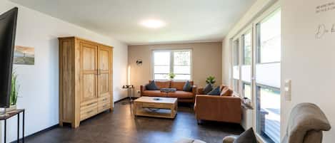 A spacious living room with a large wooden cabinet, a leather sofa, a coffee table, and a television.