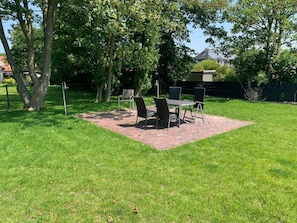A patio area with a brick table and chairs, surrounded by a grassy lawn and trees.