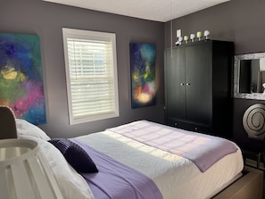 A bedroom with a bed, a wardrobe, and abstract paintings on the walls. - Artful Cottage Mtn. Retreat - 55 or over (Waynesville)