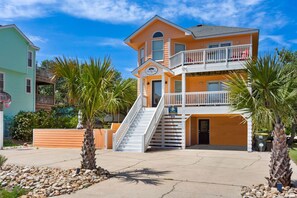 A multi-story hotel with a balcony on the second floor, a staircase leading to the entrance, and a sign indicating the name and address. - The Silly Geese: Pool Hot Tub Games, Walk to Beach (Corolla)