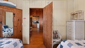 A cozy room with wooden walls, a bed with a checkered quilt, a wicker chair, and a white dresser. - Oceanfront, dog friendly, walkway to beach, cozy historic cottage- Island Dancer (Nags Head)
