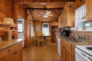 A wooden kitchen with a dining area, a ceiling fan, and a kitchen island. - Oceanfront, dog friendly, walkway to beach, cozy historic cottage- Island Dancer (Nags Head)