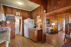 A kitchen with wooden walls, a refrigerator, a stove, and a dining area with a table and chairs. - Oceanfront, dog friendly, walkway to beach, cozy historic cottage- Island Dancer (Nags Head)