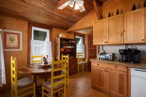 A wooden interior with a dining table, chairs, a kitchen area with cabinets, a coffee maker, and a toaster.