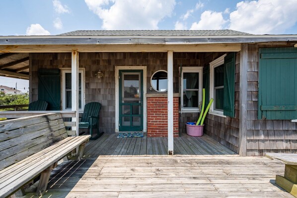 A wooden porch with a bench, a door, and a brick wall.