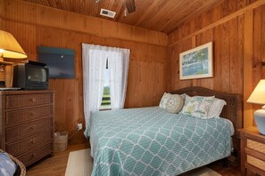 A wooden-paneled room with a bed, a dresser, a television, and a painting on the wall.