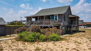 A wooden house with a porch and a staircase leading to the main floor. - Oceanfront, dog friendly, walkway to beach, cozy historic cottage- Island Dancer (Nags Head)