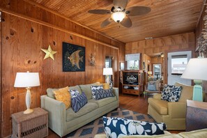 A cozy living room with wooden walls, a ceiling fan, and a television.