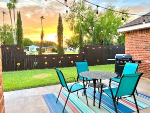 An outdoor patio with a round table and four chairs, a barbecue grill, and a string of lights.