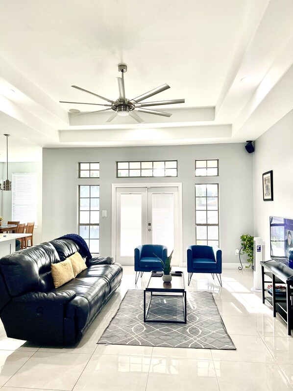 A spacious living room with a black leather sofa, two blue armchairs, a coffee table, and a ceiling fan.