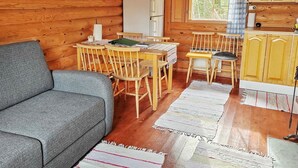 A cozy cabin interior with a sofa, wooden dining table, chairs, a refrigerator, and a window with a view of greenery. - Vacation home Ainola by Interhome (Joutsa)