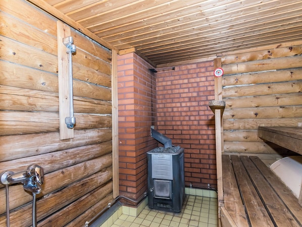 A wooden cabin interior with a brick fireplace, a metal door, and a bench.